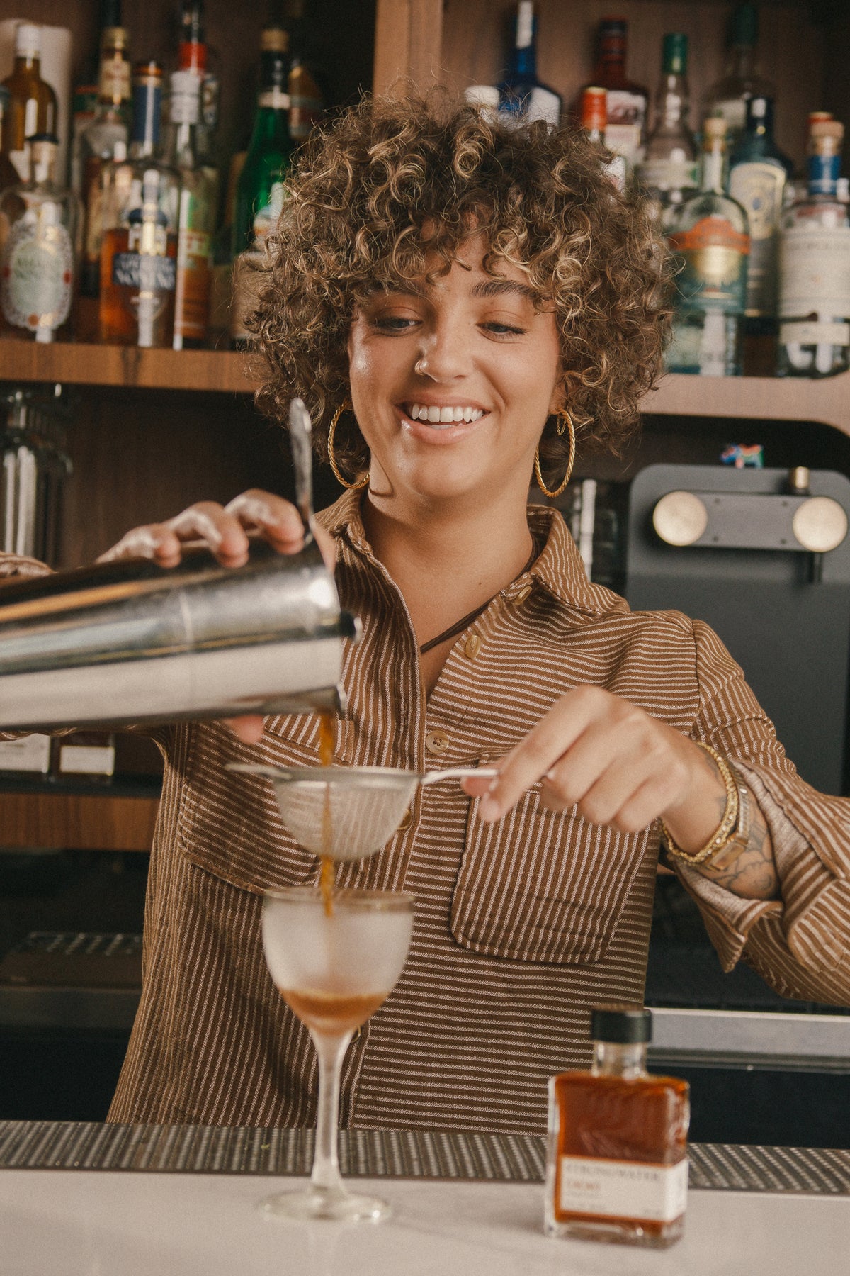 woman pouring a cocktail into a glass at a bar with strongwater cacao bitters