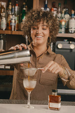 woman pouring a cocktail into a glass at a bar with strongwater cacao bitters