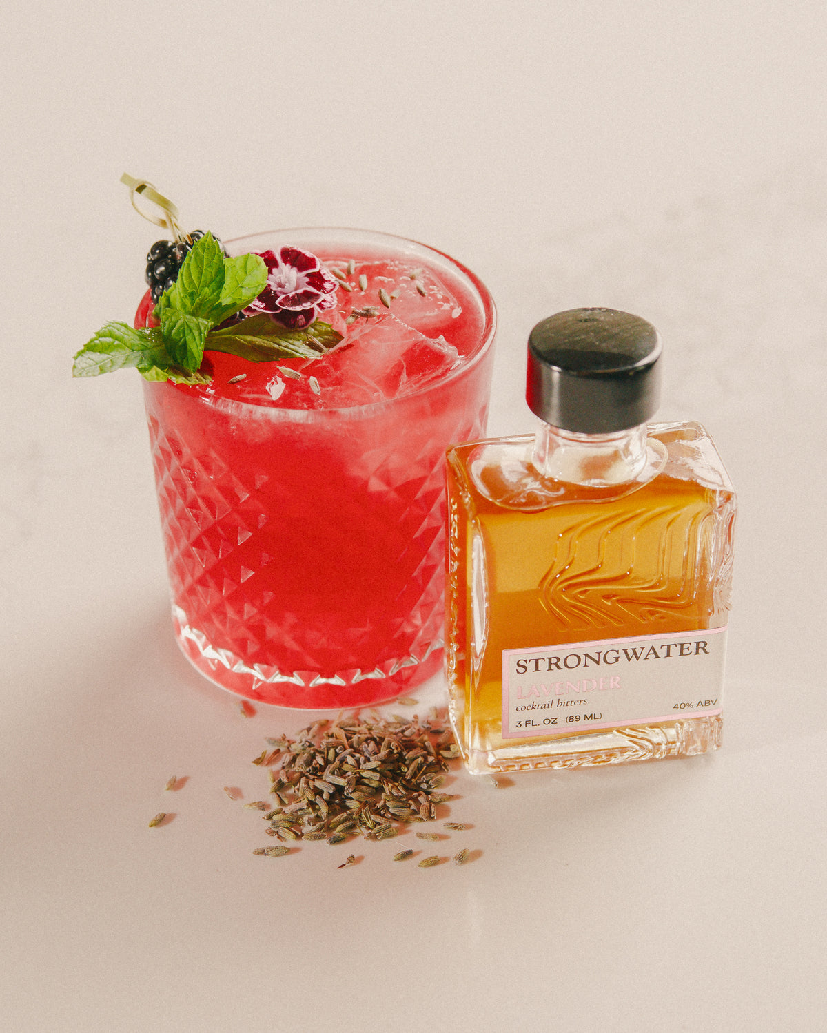 red cocktail with garnish and a bottle of strongwater lavender bitters on a light background